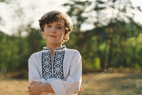 Preview: A boy smiles confidently while standing in a sunlit field, wearing a traditional embroidered shirt