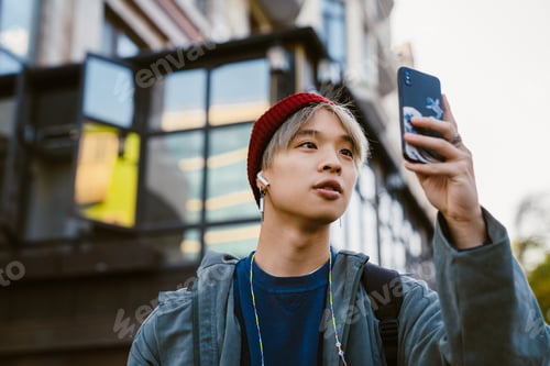 Preview: Asian boy taking photo on mobile phone at city street
