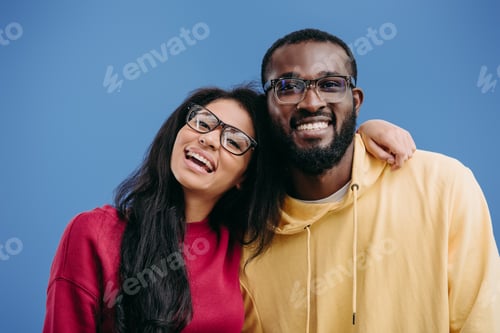 Preview: portrait of happy african american couple in eyeglasses looking at camera isolated on blue