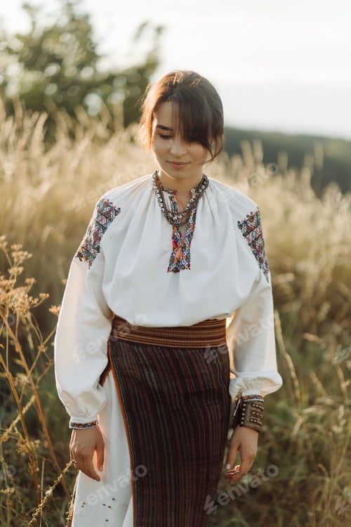 Preview: Young woman in traditional national embroidered shirt and skirt on nature at sunset.