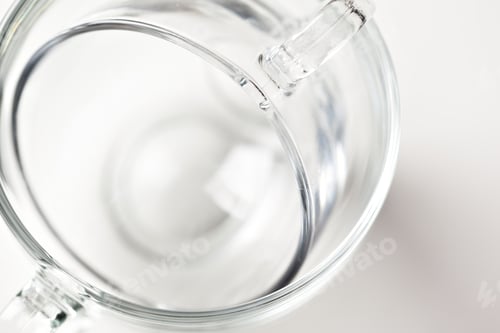 Preview: Clear glass cup sits on a white surface with a soft focus around it in bright light