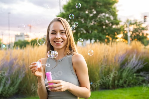Preview: A cheerful young woman blowing soap bubbles in a city garden.