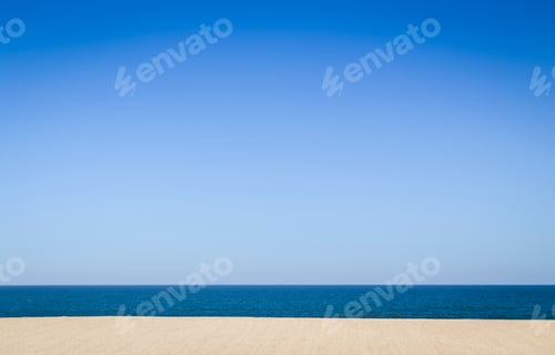 Preview: An empty sandy beach and ocean, view out to sea under a clear blue sky.