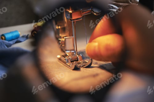 Preview: Crop hand putting thread in needle behind magnifying glass