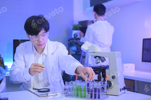 Preview: Scientist wearing safety goggles compares green and purple liquid samples in test tubes
