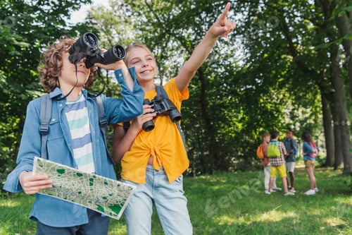 Preview: selective focus of happy kid pointing with finger near friend holding map and looking through