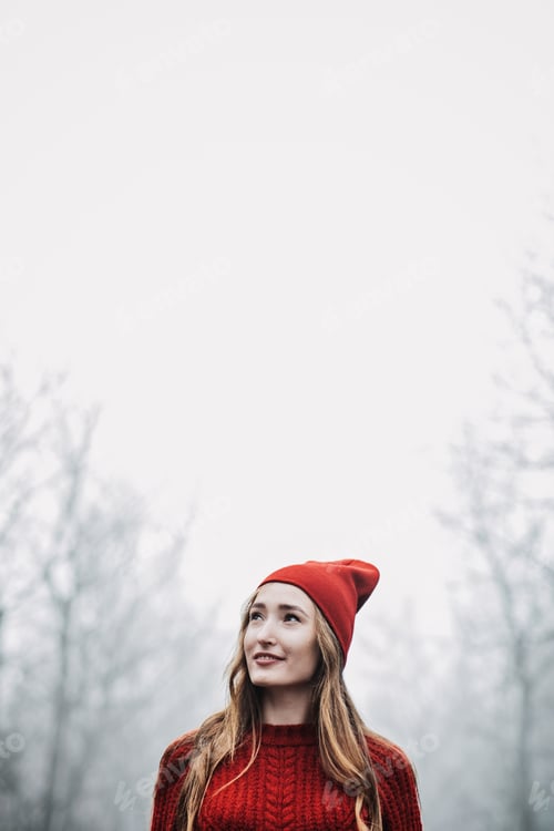 Preview: Woman in red hat and sweater walking on foggy mystical morning forest.