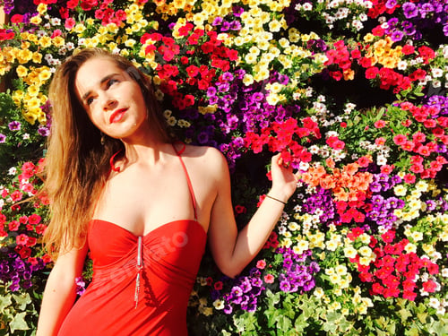 Preview: Woman in sexy red bathing suit standing against wall of multicoloured flowers