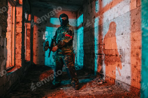 Preview: confident male paintball player in goggle mask and camouflage holding paintball gun in abandoned