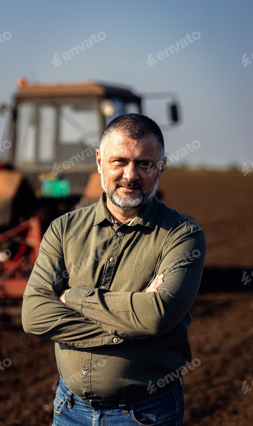 Preview: Portrait of satisfied mature farmer standing in field preparing to cultivate the land with a tractor