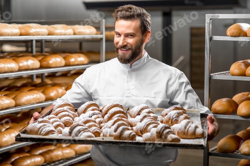Preview: Handsome baker holding tray full of freshly baked croisants