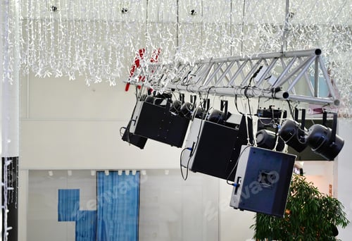 Preview: Modern audio equipment suspended from a truss in a spacious indoor venue during an event setup