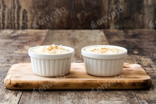 Preview: Creamy rice pudding with cinnamon in white ramekins on rustic wooden board