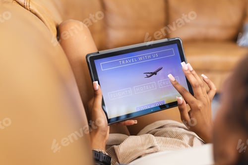 Preview: A young African American woman browses travel options on a tablet, booking a vacation online