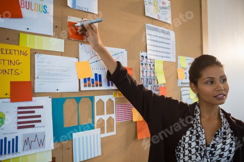 Preview: Female executive pointing at sticky note on bulletin board