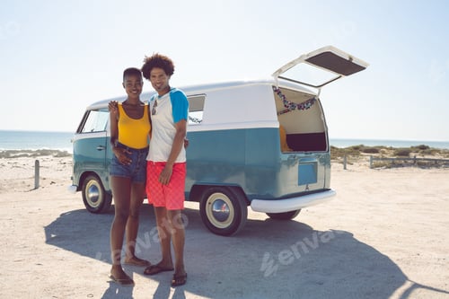 Preview: Front view of diverse couple looking at camera while standing near camper van at beach