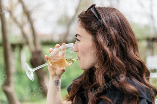Preview: Woman drinking white wine, while sitting outside.