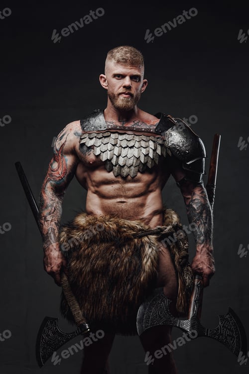 Preview: Brutal tattooed warrior wearing light armour and fur holding axes in dark studio