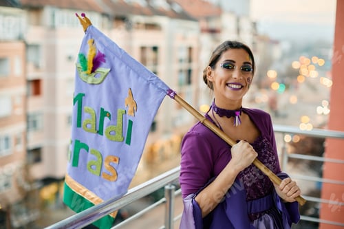 Preview: Young beautiful woman with Mardi Gras flag standing on a balcony.