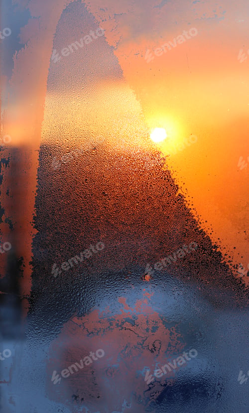 Preview: Ice pattern, water drops and sun on a window glass at dawn