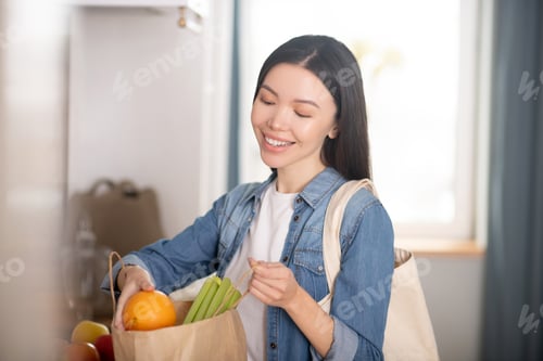 Preview: Beautiful young woman with paper bag of vegetables and fruits.
