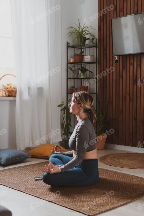 Preview: Sportive young woman practices yoga at home in a cozy room.