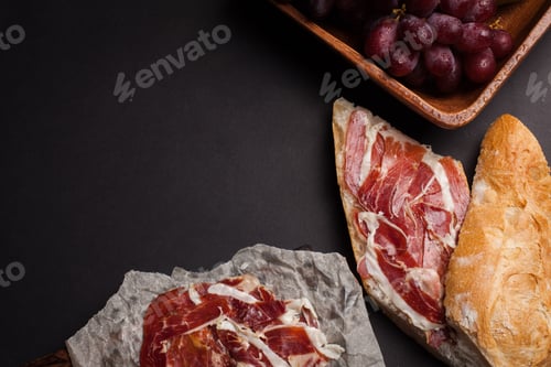 Preview: Jamon Iberico with white bread, olives on toothpicks and fruit on a dark background.