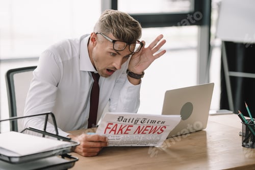 Preview: selective focus of emotional businessman touching glasses while reading newspaper with fake news