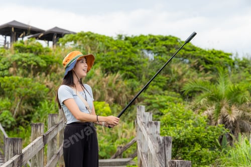 Preview: Woman walk along the hiking trail with hold with 360 camera to take photo and video at countryside