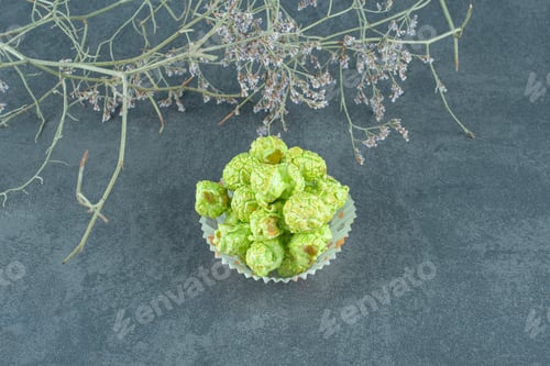 Preview: Neat stack of green popcorn candy next to decorative branches on marble background