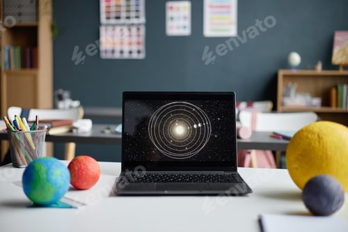 Preview: Laptop Displaying Solar System Diagram Surrounded by Planet Models in Classroom
