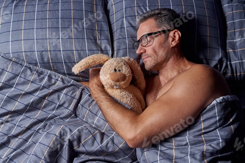 Preview: A man sleeps in a bed with a stuffed rabbit