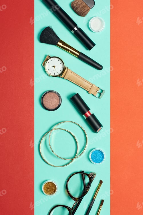 Preview: Top view of mascara, watch, lipstick, bracelets, eyeshadow, blush, glasses and cosmetic brushes