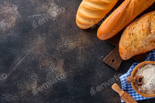 Preview: Various crispy breads and buns, wheat flour and ears on brown old concrete background table. Top vie