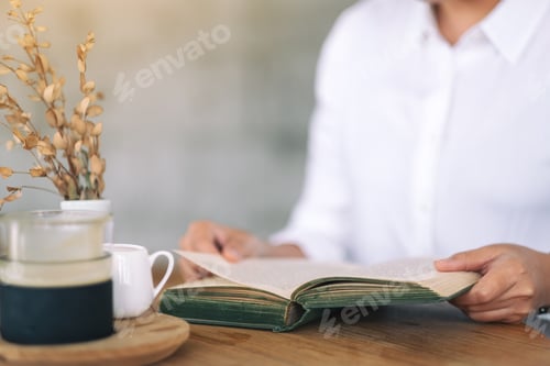 Vista previa: Closeup image of a woman holding and reading a vintage novel book on wooden table
