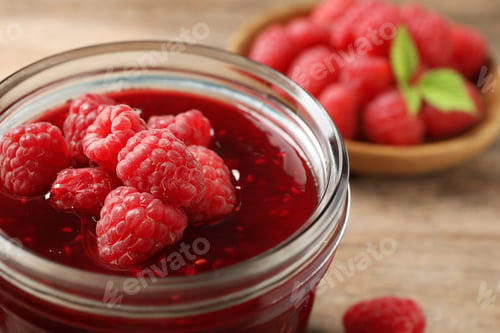 Preview: Glass jar of sweet jam with ripe raspberries on wooden table, closeup