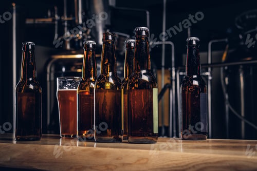 Preview: Bottles and glass of craft beer on wooden bar counter at the indie brewery.