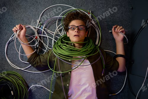 Preview: Frustrated overwhelmed teenager IT engineer lying on floor wrapped in wire