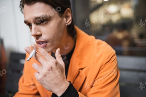 Preview: Man in orange jacket smoking blurred cigarette outdoors