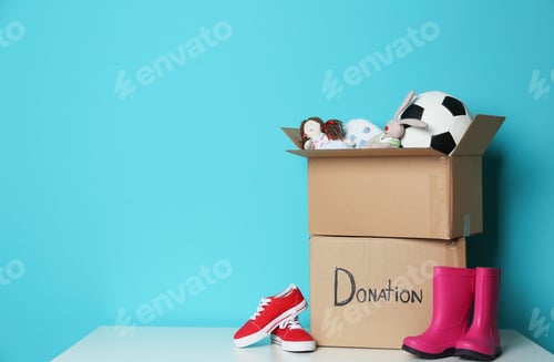 Preview: Donation boxes with toys and shoes on table against color background. Space for text
