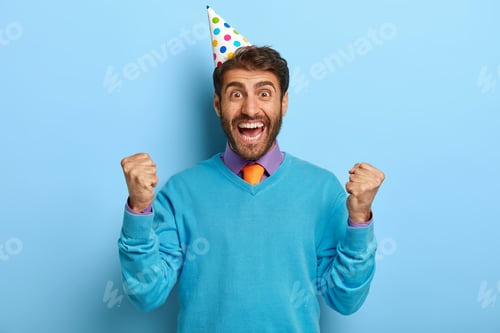 Preview: Studio photo of overjoyed party man clenches fists with satisfaction, happy to get desirable present