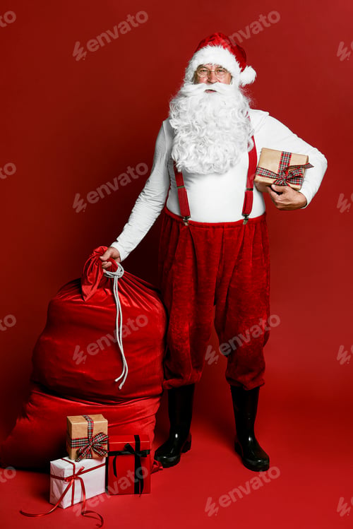 Preview: Caucasian Santa Claus standing on red background with Christmas presents