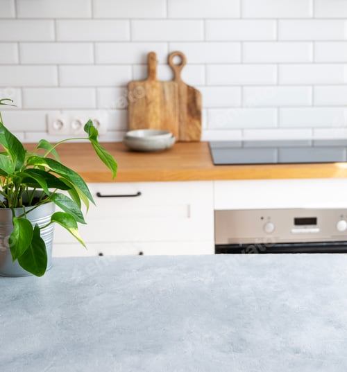 Preview: Wooden blue table top with flower pot against blurred white kitchen with cutting board