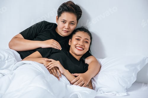 Preview: Two female couples cuddled together in bed.