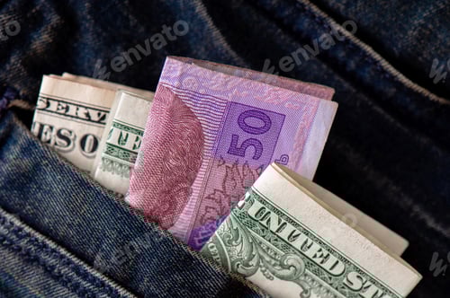 Preview: Folded Ukrainian hryvnia and American dollars protrude from the pocket of jeans close-up.