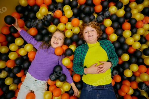 Preview: Charming funny children lying in dry pool with colorful balls