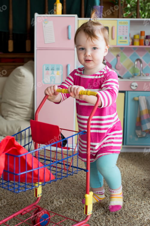 Preview: Portrait of young girl pushing toy supermarket trolley