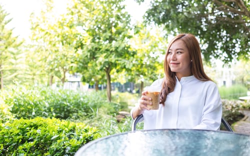 Preview: Portrait image a young asian woman holding and drinking iced coffee in the outdoors