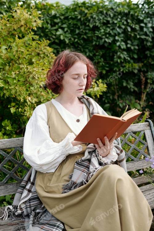 Preview: Youthful girl in casualwear reading book while sitting on bench in the garden
