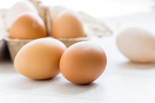 Preview: Brown and white organic chicken eggs in a brown paper box placed on a white wooden table